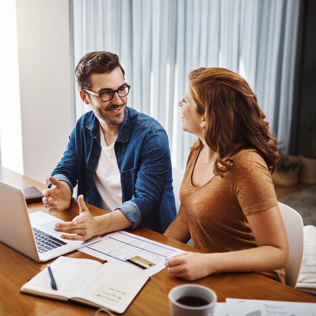 A couple in happy mood discussing something with their laptop open on a table.