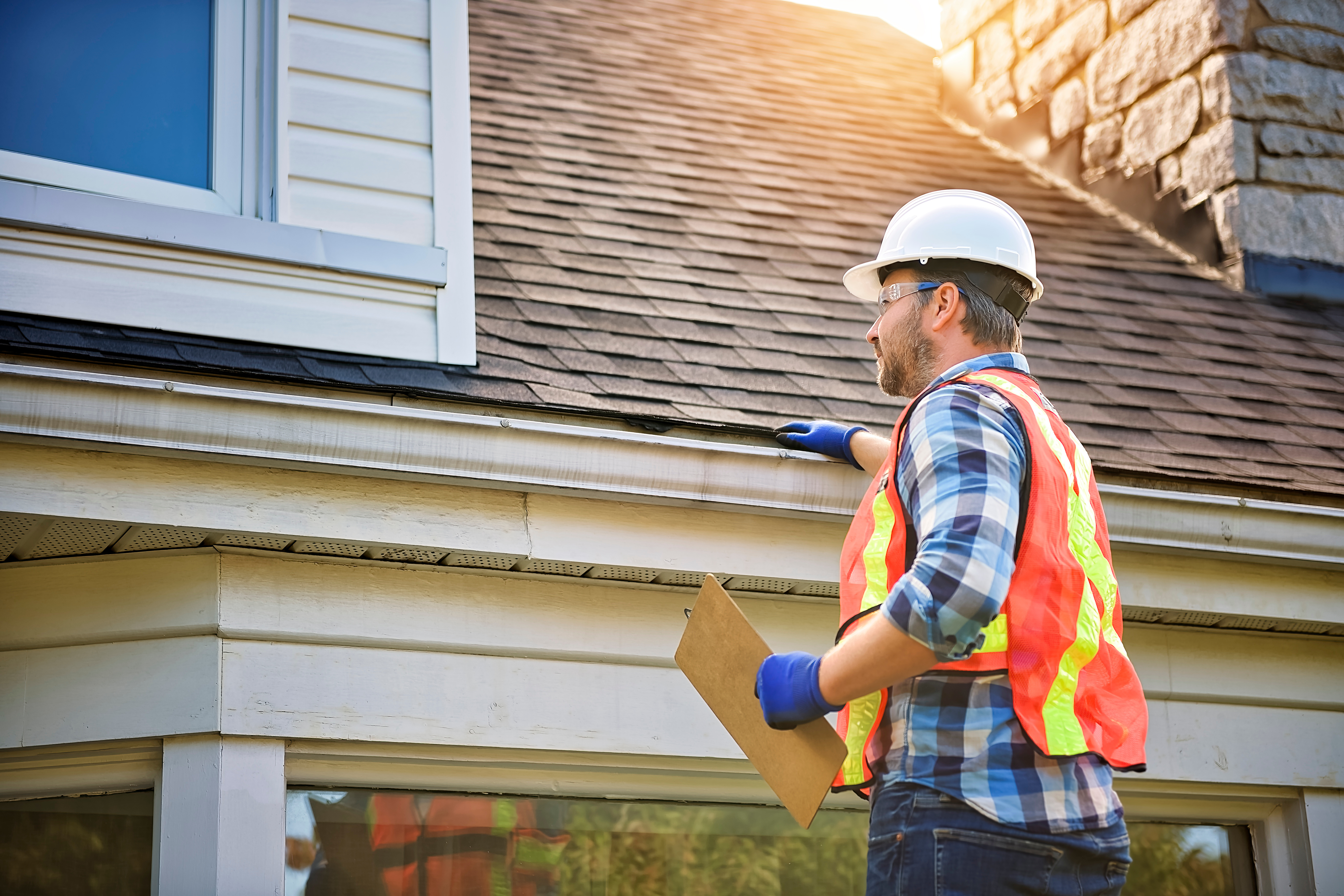 A home inspector with safety jacket and gloves doing inspection of the roof of a home. 