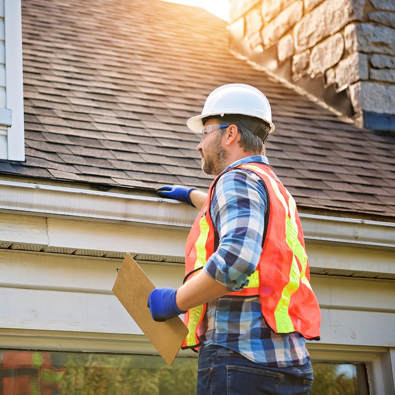 A home inspector with safety jacket and gloves doing inspection of the roof of a home.