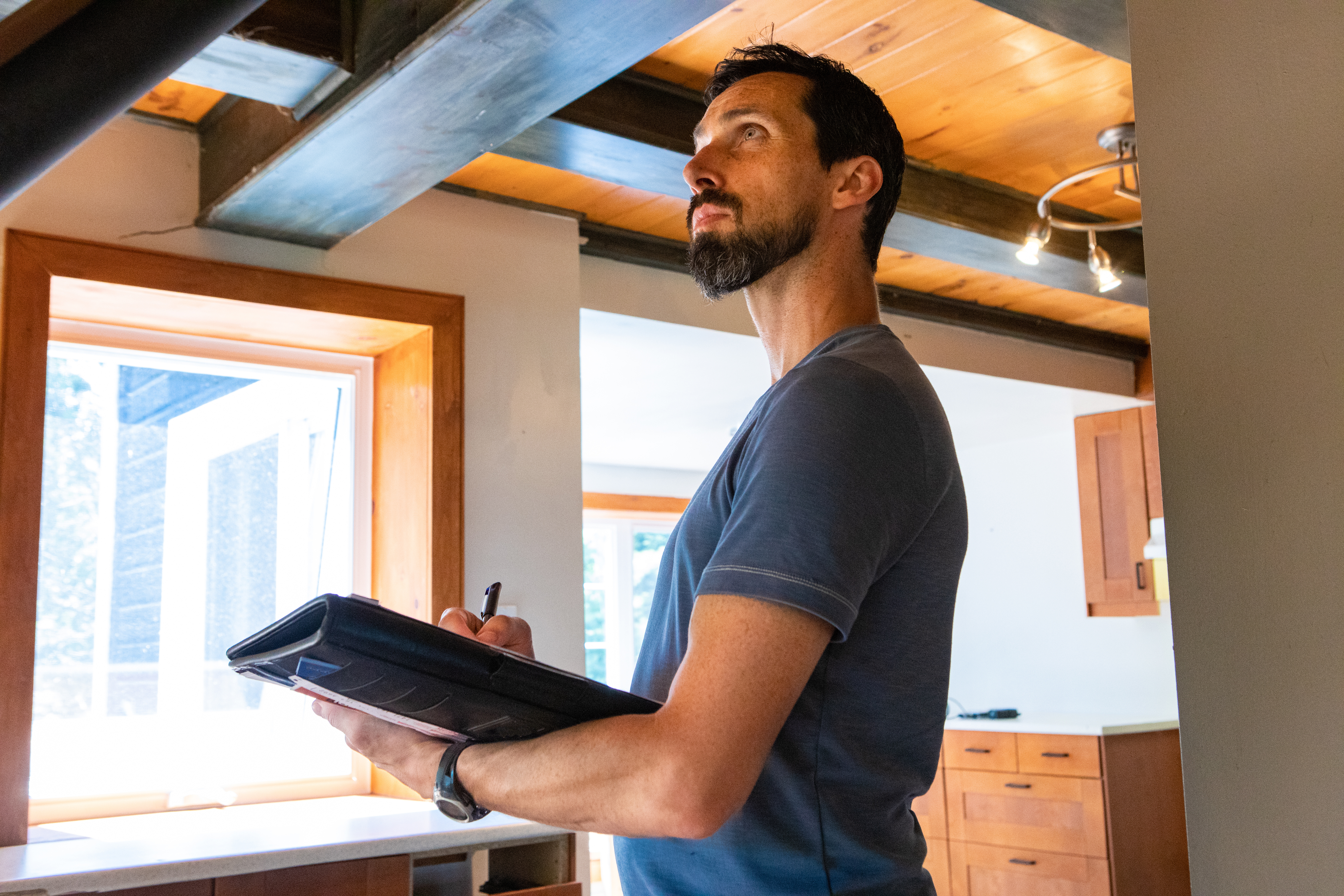 An appraiser looking at the ceiling of a constructed property, holding a paper and pen in his hands.