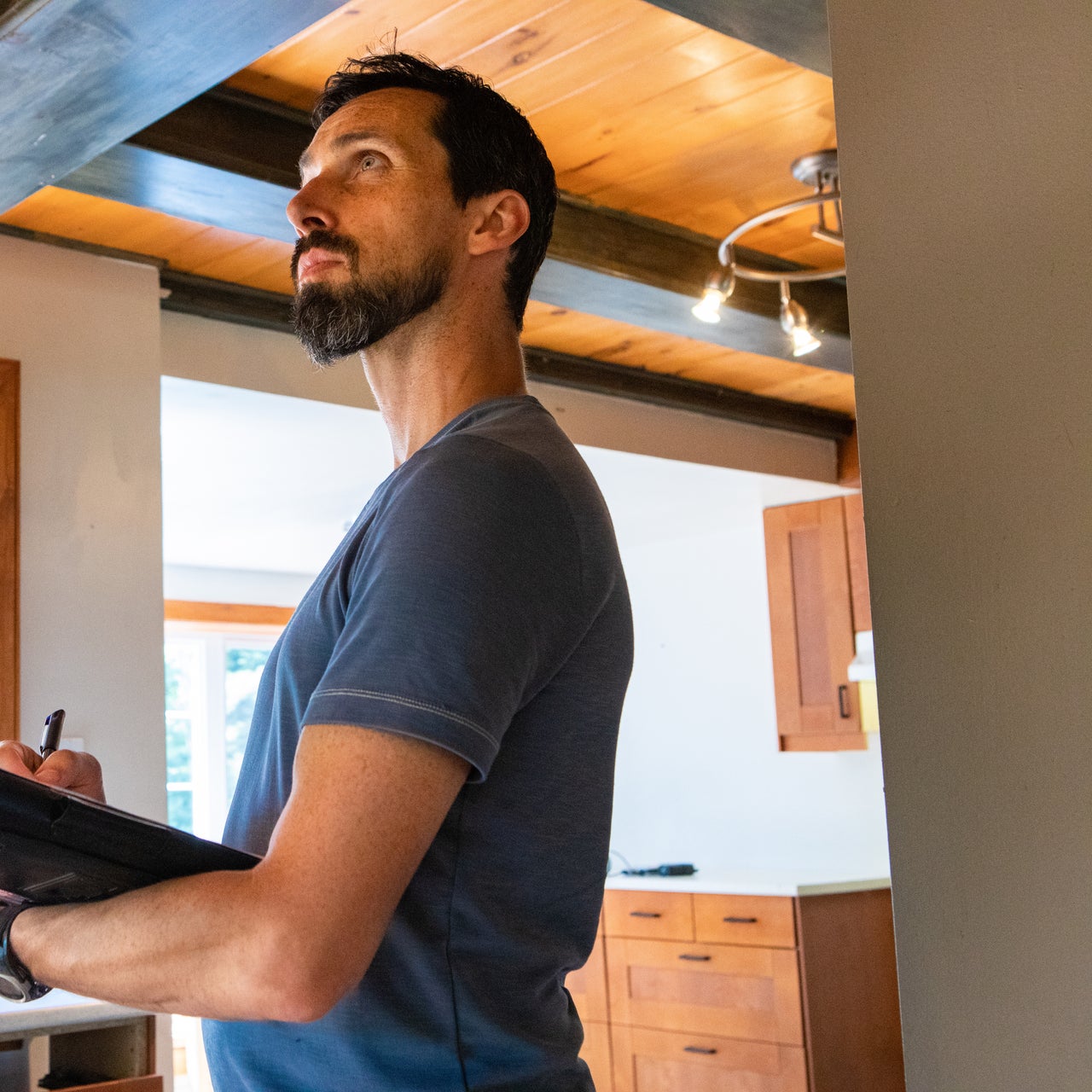 An appraiser looking at the ceiling of a constructed property, holding a paper and pen in his hands.