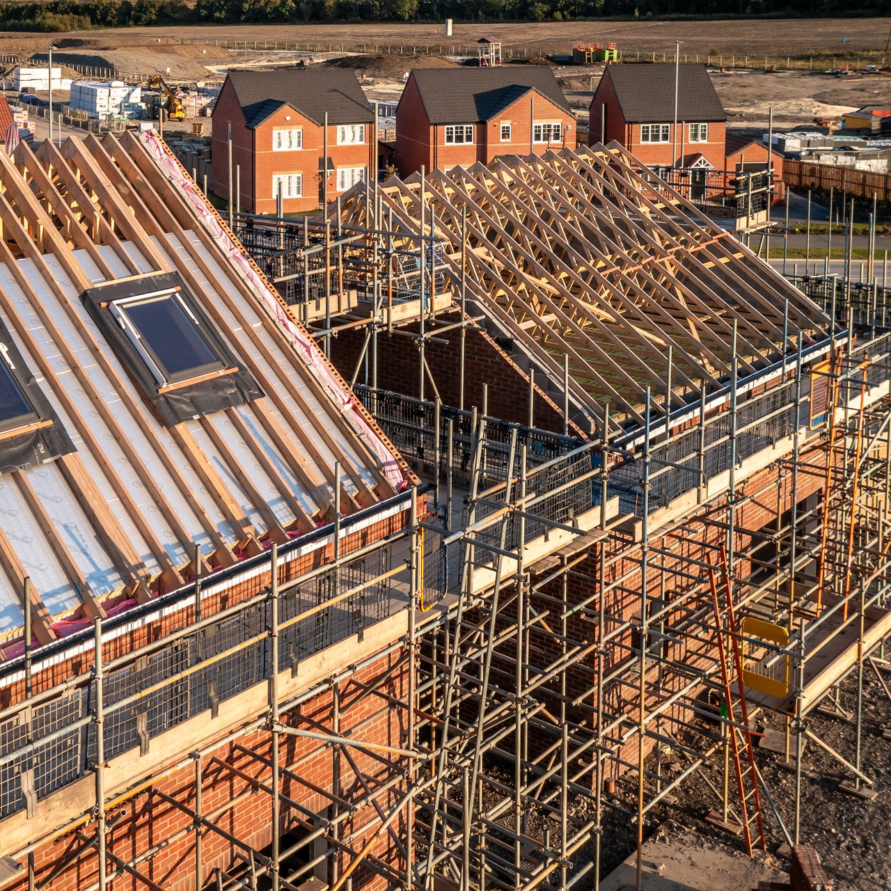 Aerial view of a roof under construction with beams and apex supporting exterior skylight windows on a new build house surrounded by scaffolding on a construction site.