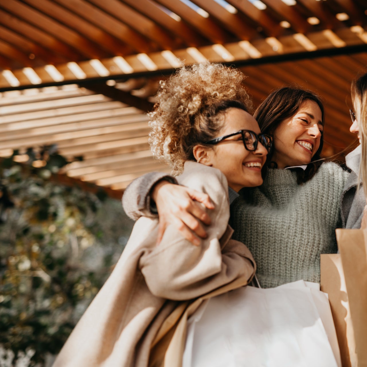 Three happy friends embracing with retail bags, celebrating a successful day of shopping.