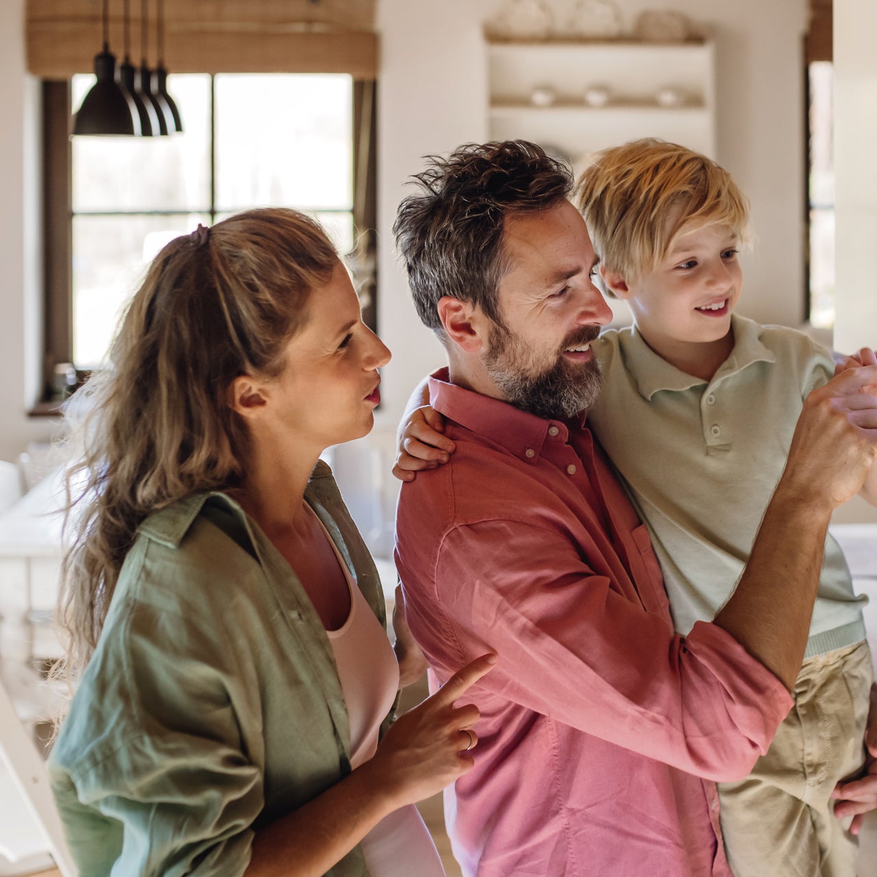 A family of three looks at a smart home display panel on a wall.