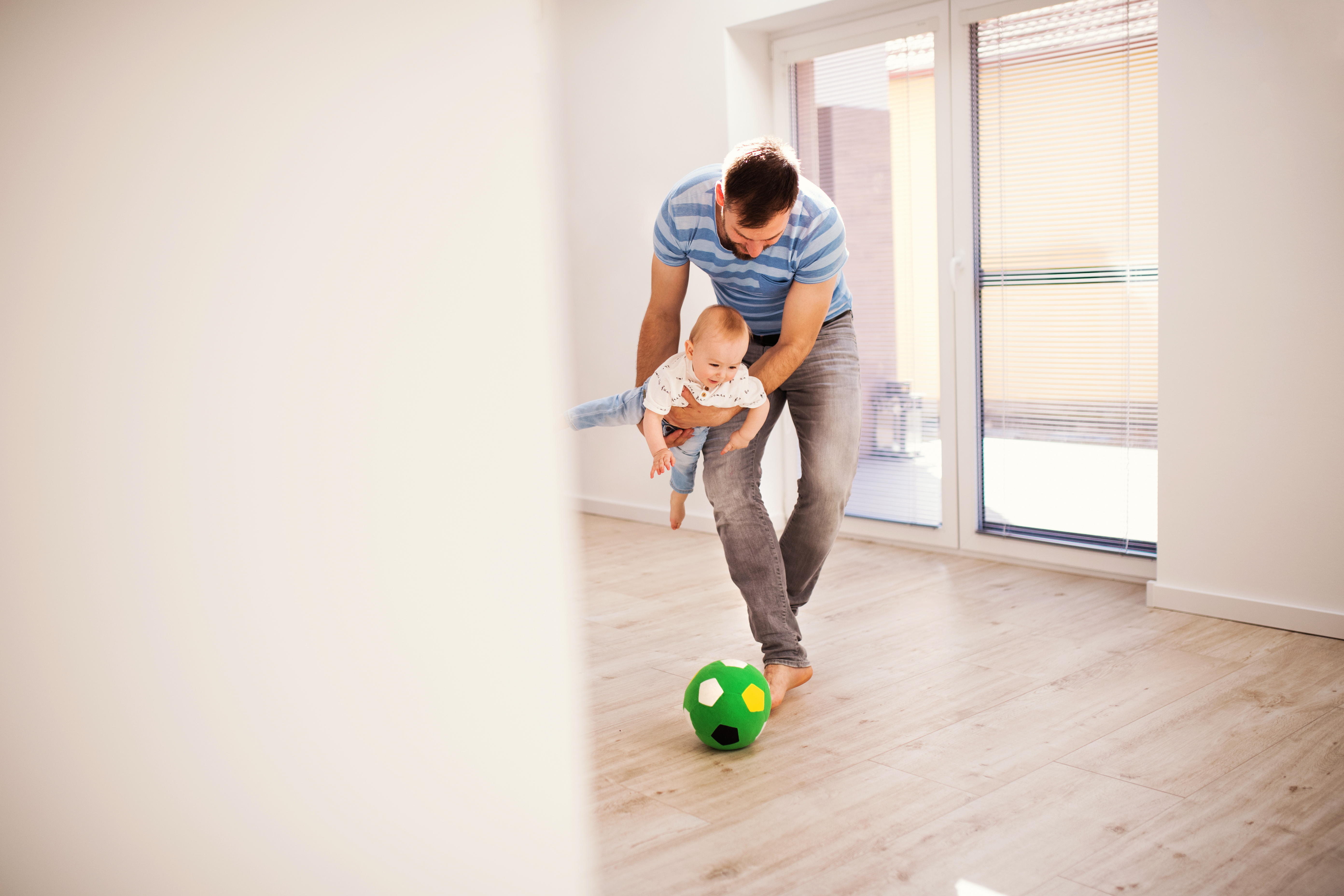 Dad playing soccer with baby in a house.