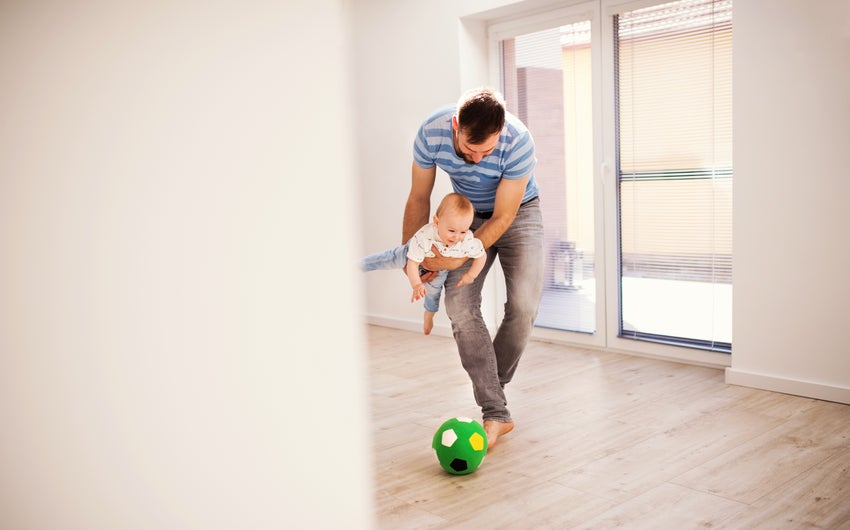 Dad playing soccer with baby in a house.