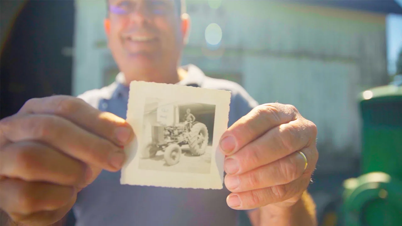 A man holding an old black and white photo with a kid sitting on a tractor
