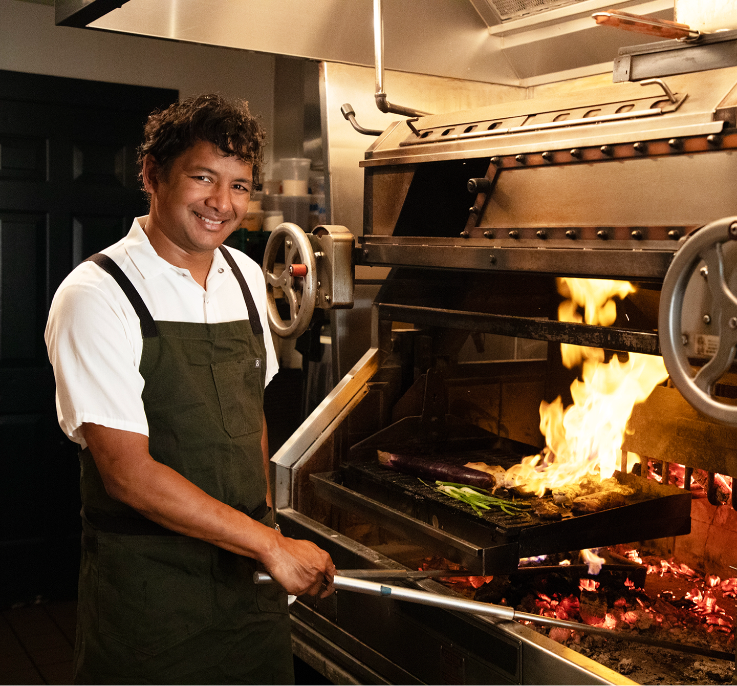 A man cooking on multiple grills in a restaurant kitchen