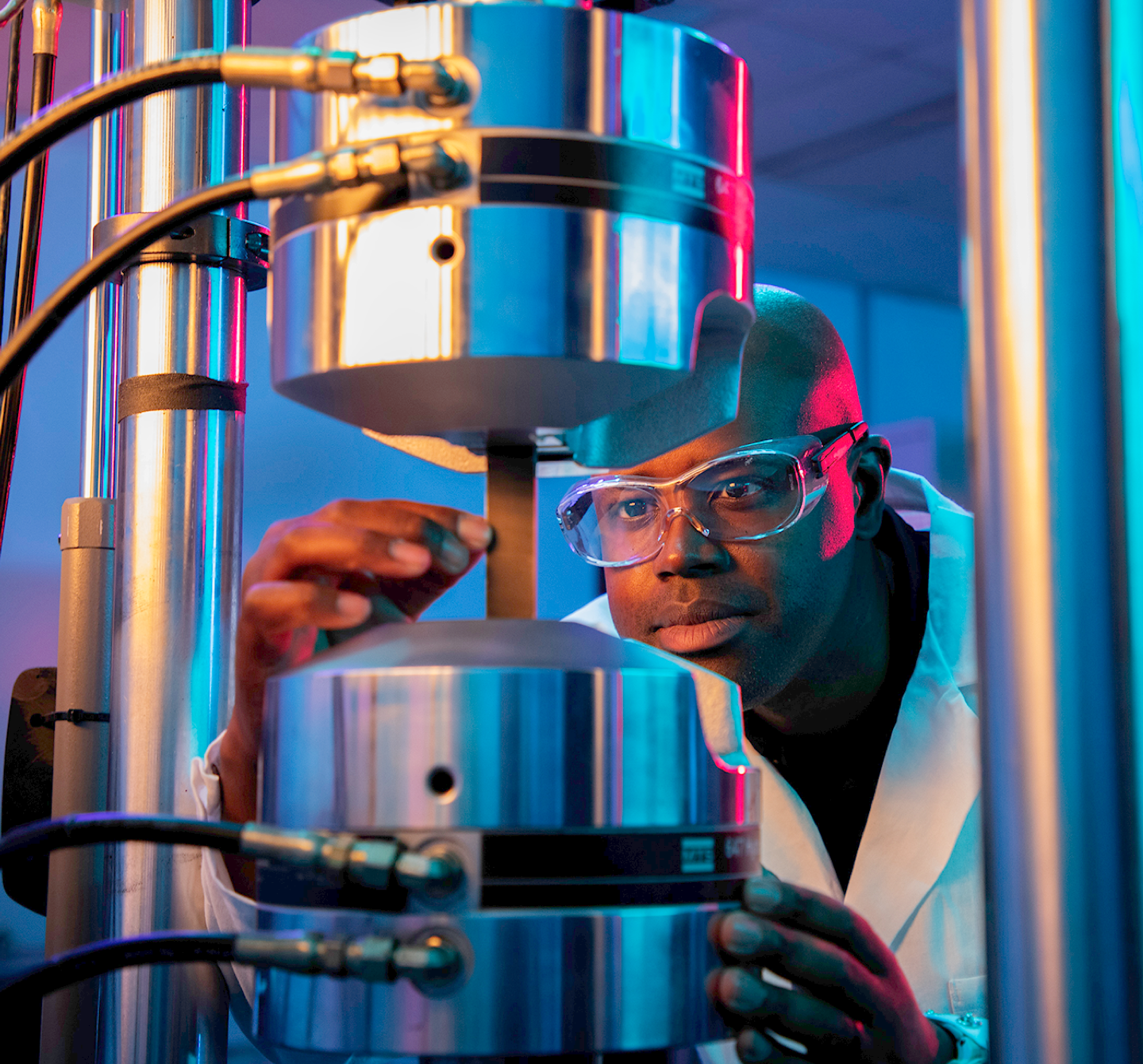 A man in a white coat and goggles looking at a machine