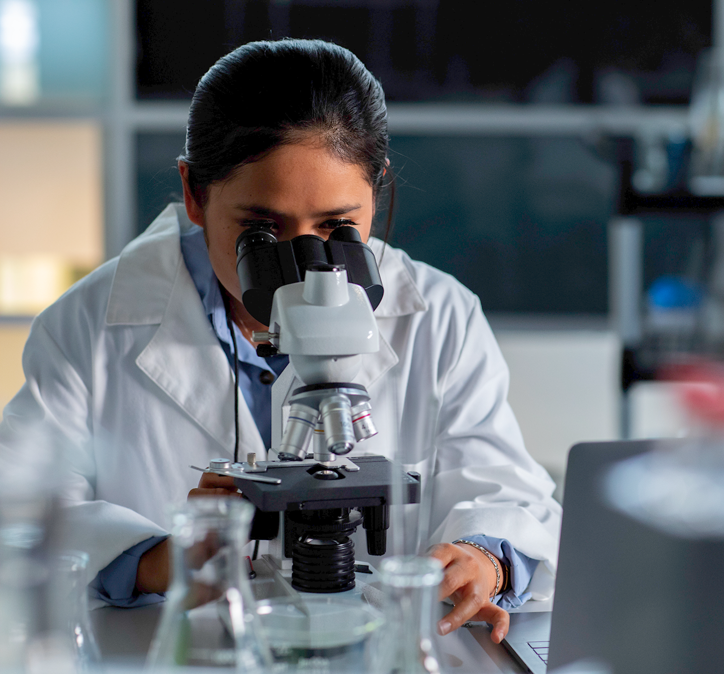 A woman in a white coat looking into a microscope