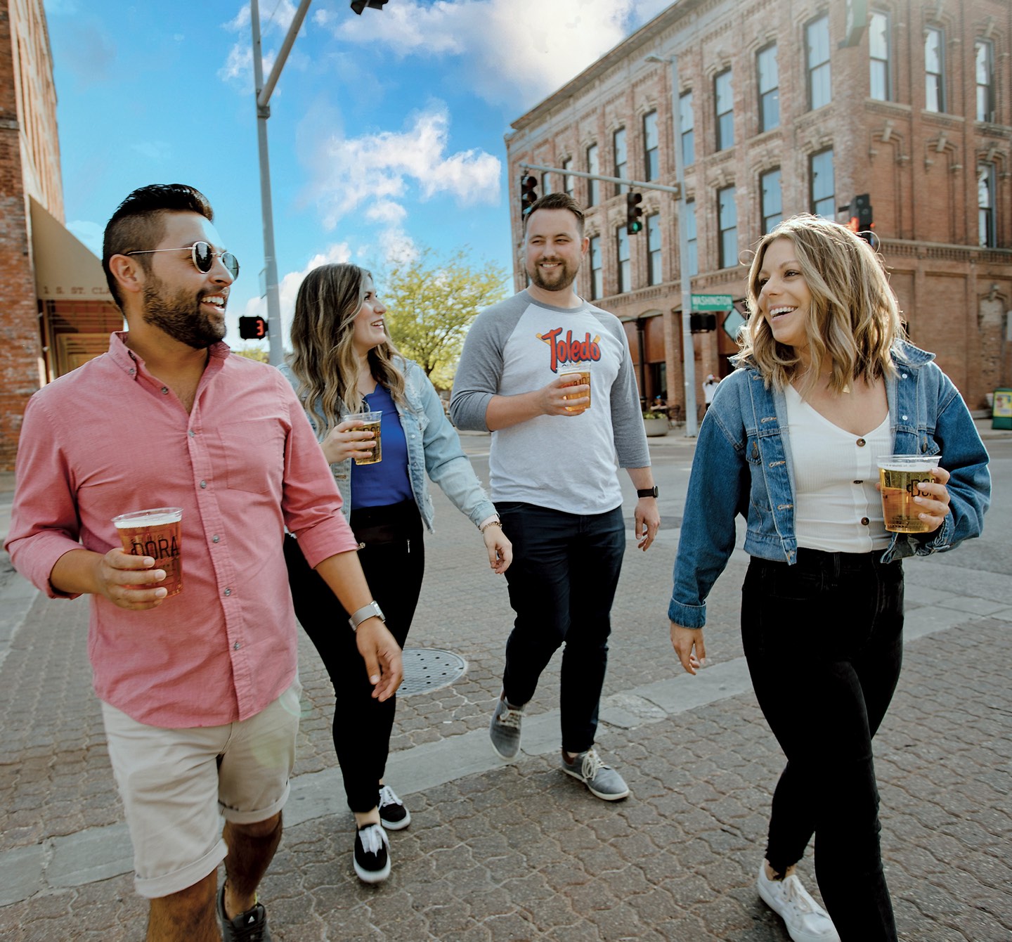 4 friends walking down an urban street with beers in hand