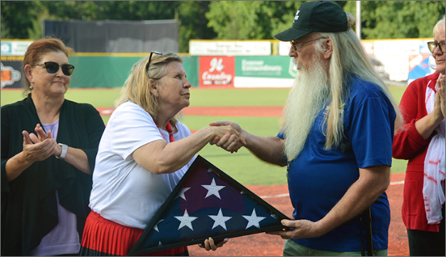 A woman accepting an American flag from a man and shaking his hand