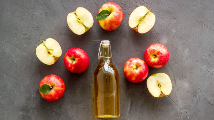 a bottle of apple cider vinegar surrounded by fresh apples
