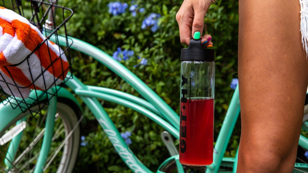 woman holding a bottle of Essential elements' Hydration in front of her bicycle