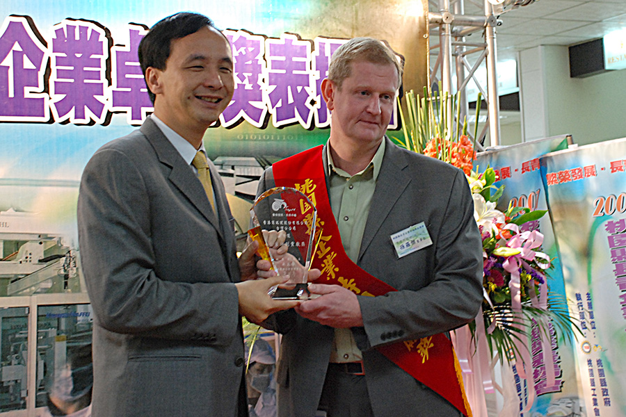 SHL Medical’s founder holding a Taiwan Excellence Award trophy at an exhibition booth.