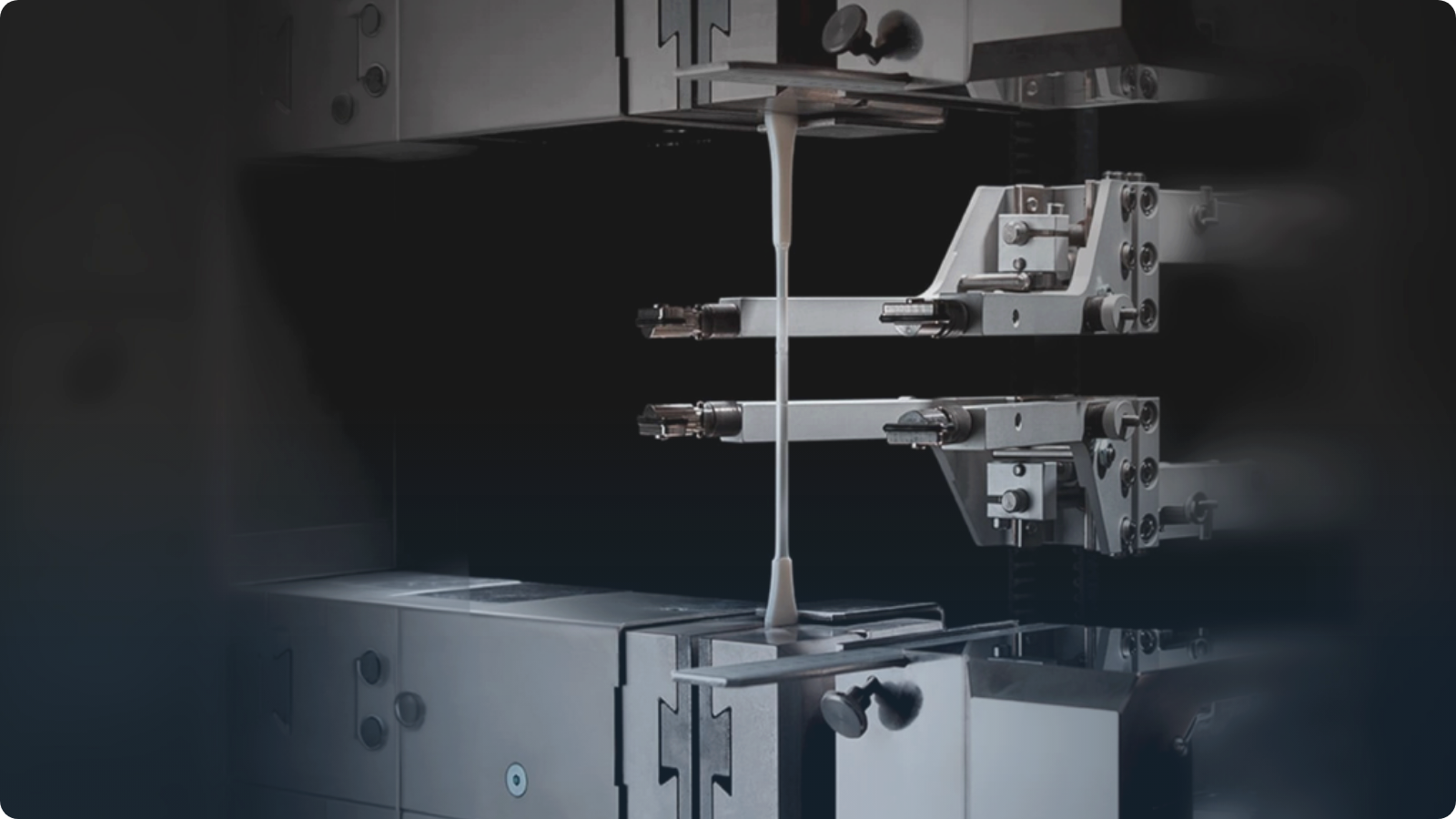 Close-up laboratory testing equipment stretching a sample of material between two metal fixtures.