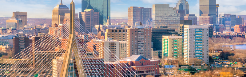 View of the Boston skyline and waterfront, featuring high-rise buildings under a blue sky. SHL Advantec will join SHL Medical at PODD 2026, highlighting drug delivery device manufacturing, autoinjector assembly, and medical device automation.