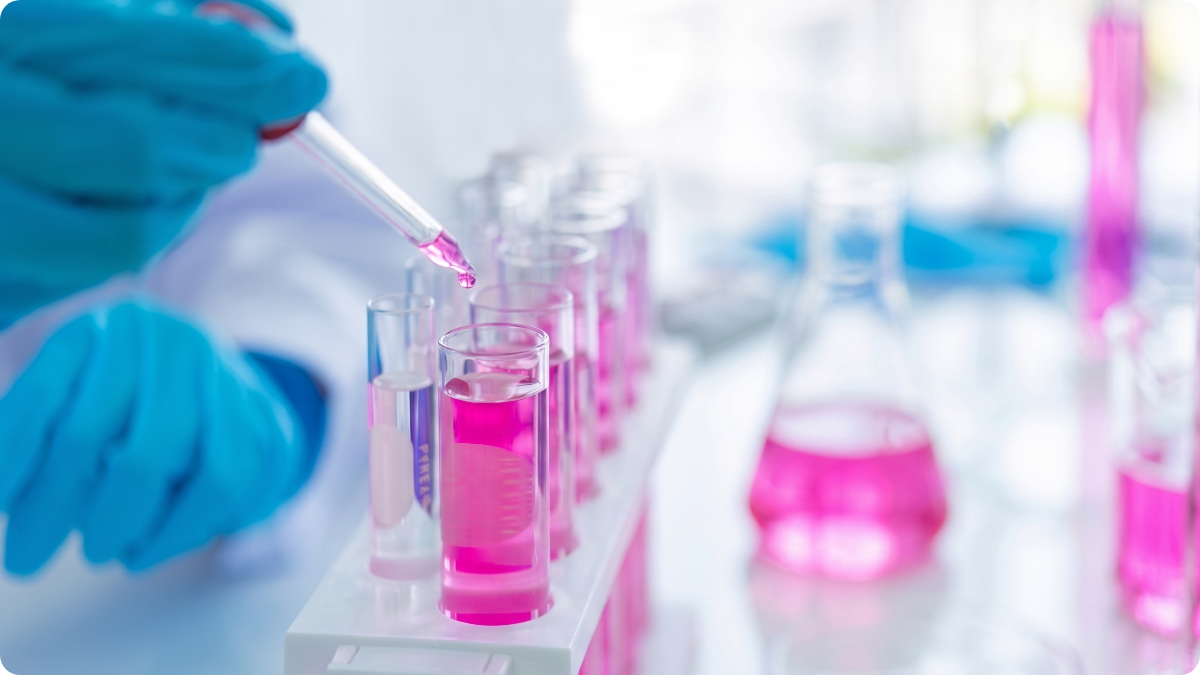 A pipette transfers pink liquid into laboratory test tubes during materials or biocompatibility analysis.