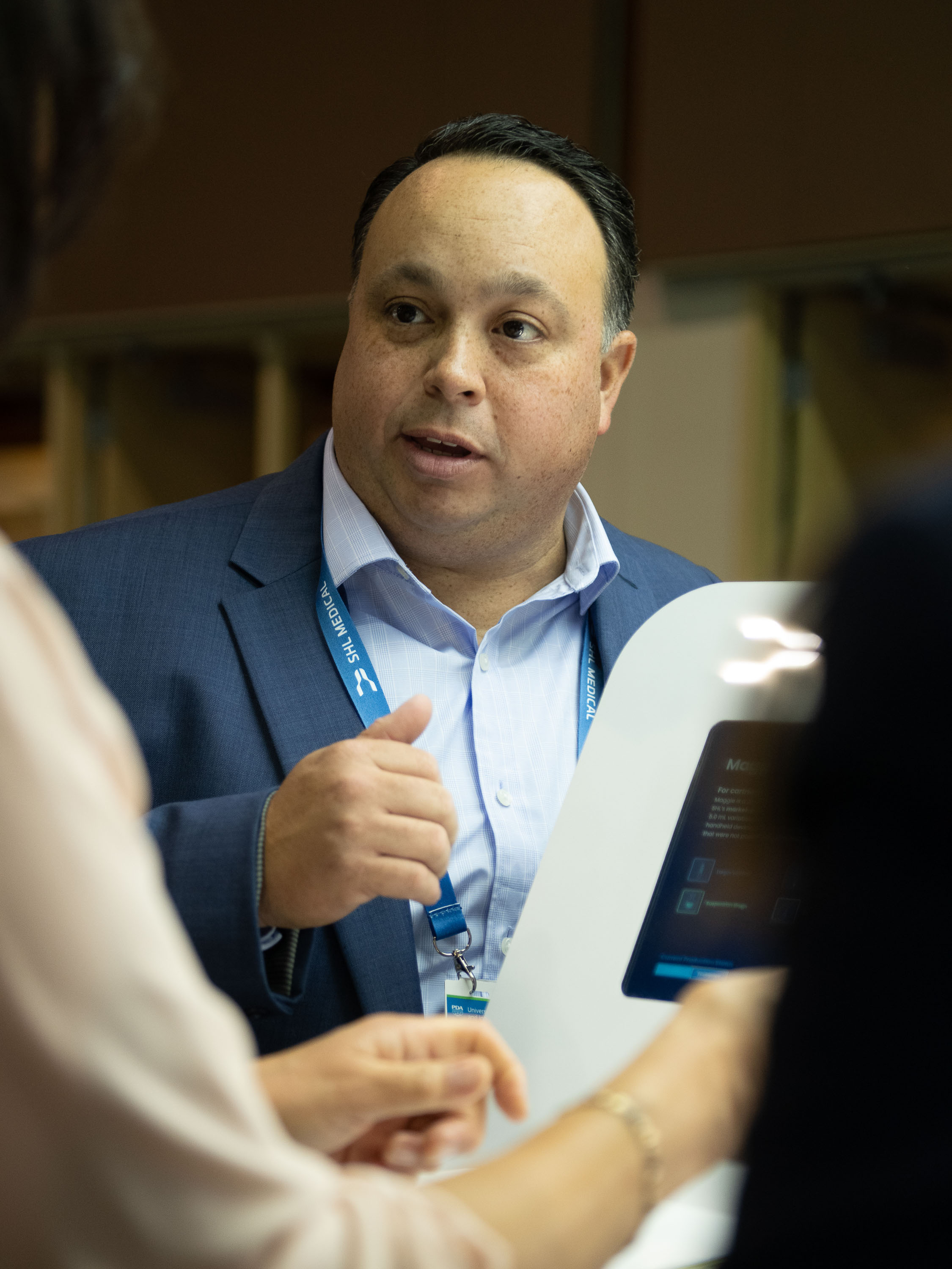 Man in a suit speaking with visitors at an event. SHL Medical’s Head of Business Development Americas highlights how the North America self-injection market drives innovations.