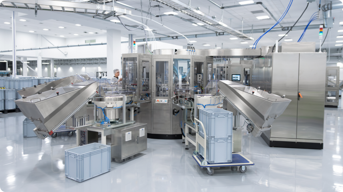 Cleanroom manufacturing floor with automated assembly equipment, stainless steel machinery, material bins, and production operators.