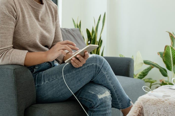 A woman sitting in her home and preparing for hurricane season by ensuring her phone is charged A woman sitting in her home and preparing for hurricane season by ensuring her phone is charged