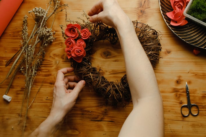 A person adding floral elements to their DIY Valentine’s Day heart-shaped wreath withroses and other small blossoms.