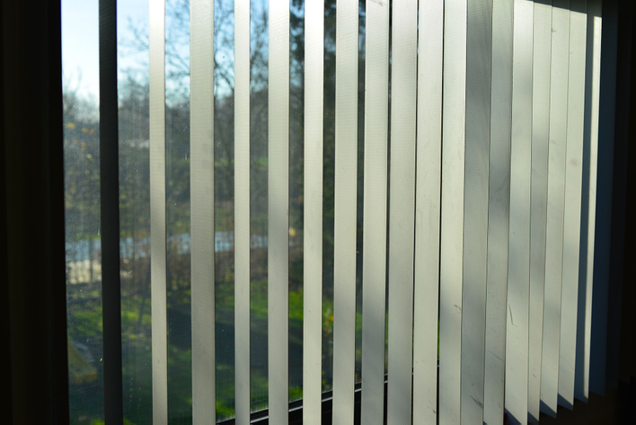 Vertical blinds in front of a large window with a pet-proof window screen.
