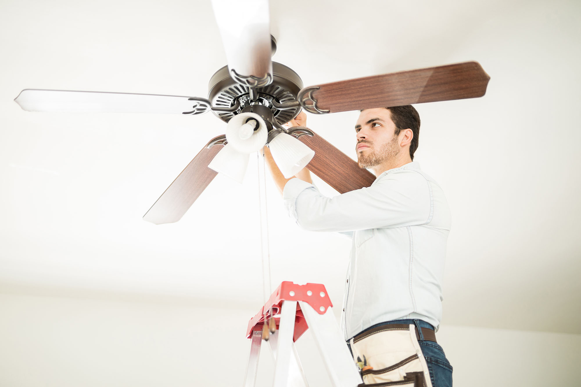 Person working on a ceiling fan to spin clockwise in the house.