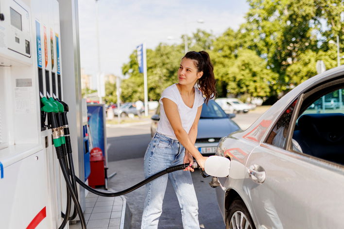 A woman filling up her car at a gas station, adding to her carbon footprint for the year.