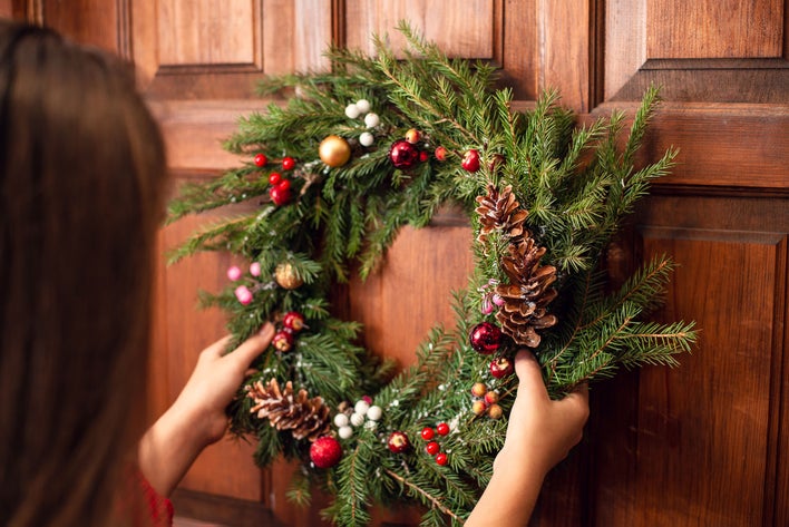 A woman hanging a wreath on a woodgrain entry door.