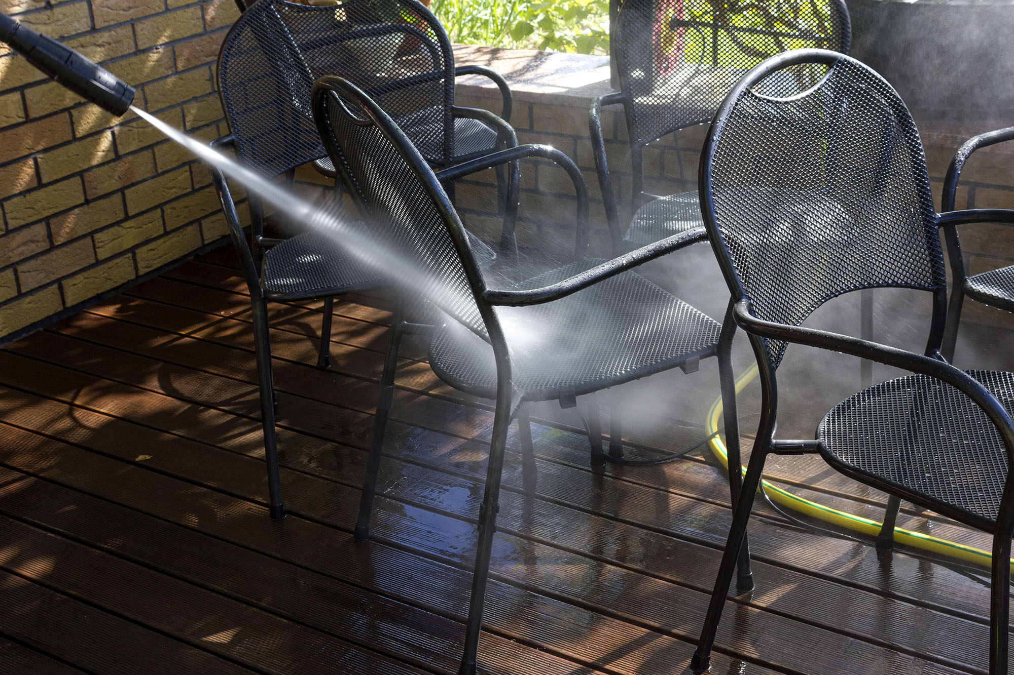 Person pressure washing outdoor patio furniture as part of summer home maintenance.