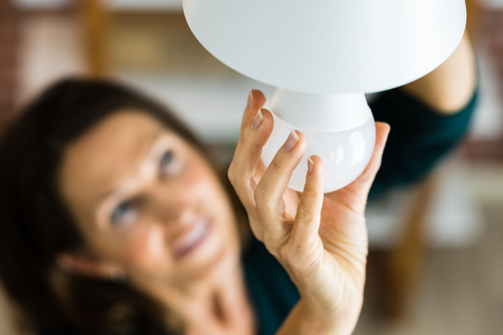 A woman replacing the bulb in a light fixture with LED.