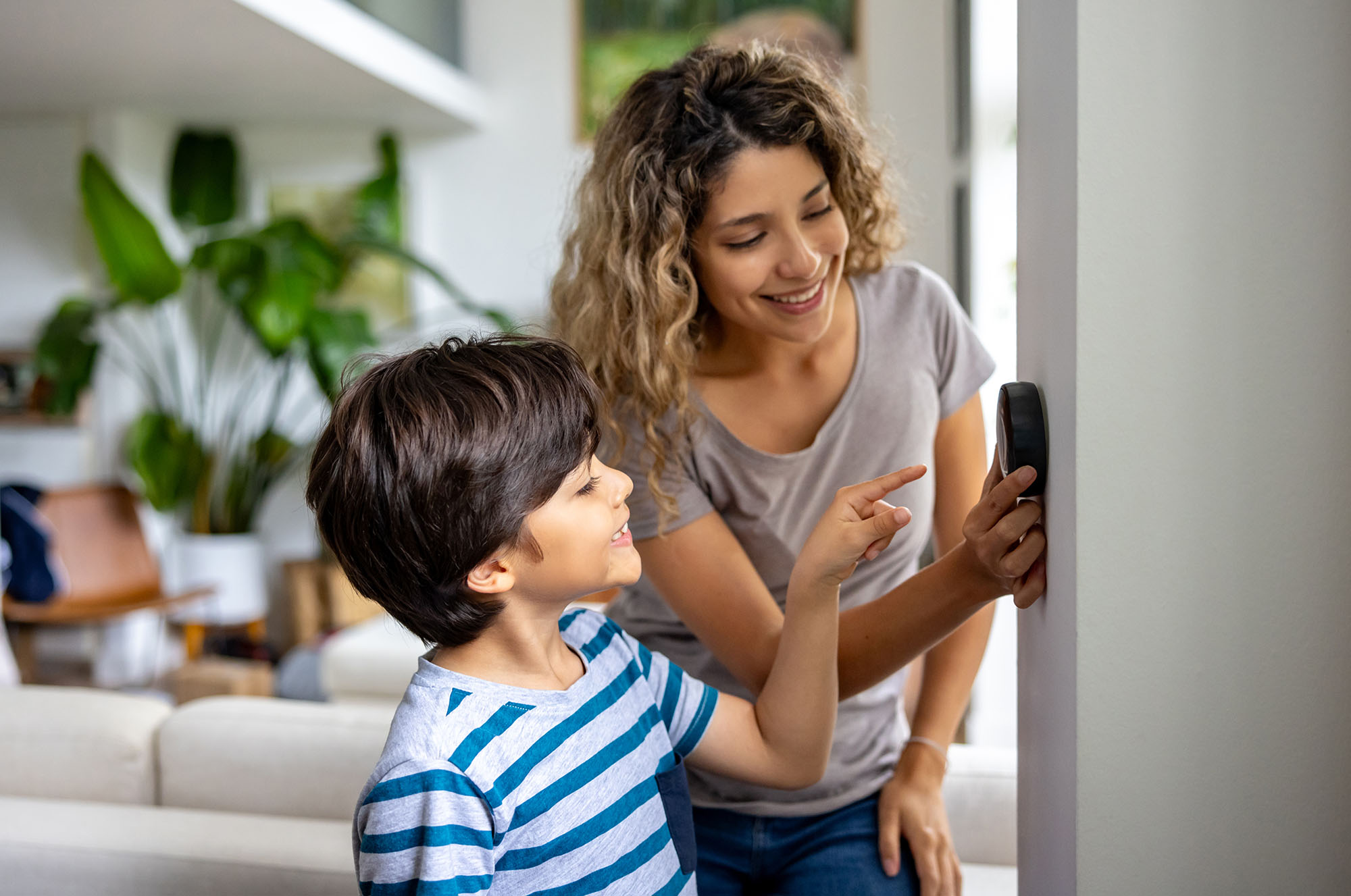 A woman and child adjusting their home thermostat to reduce carbon footprint.