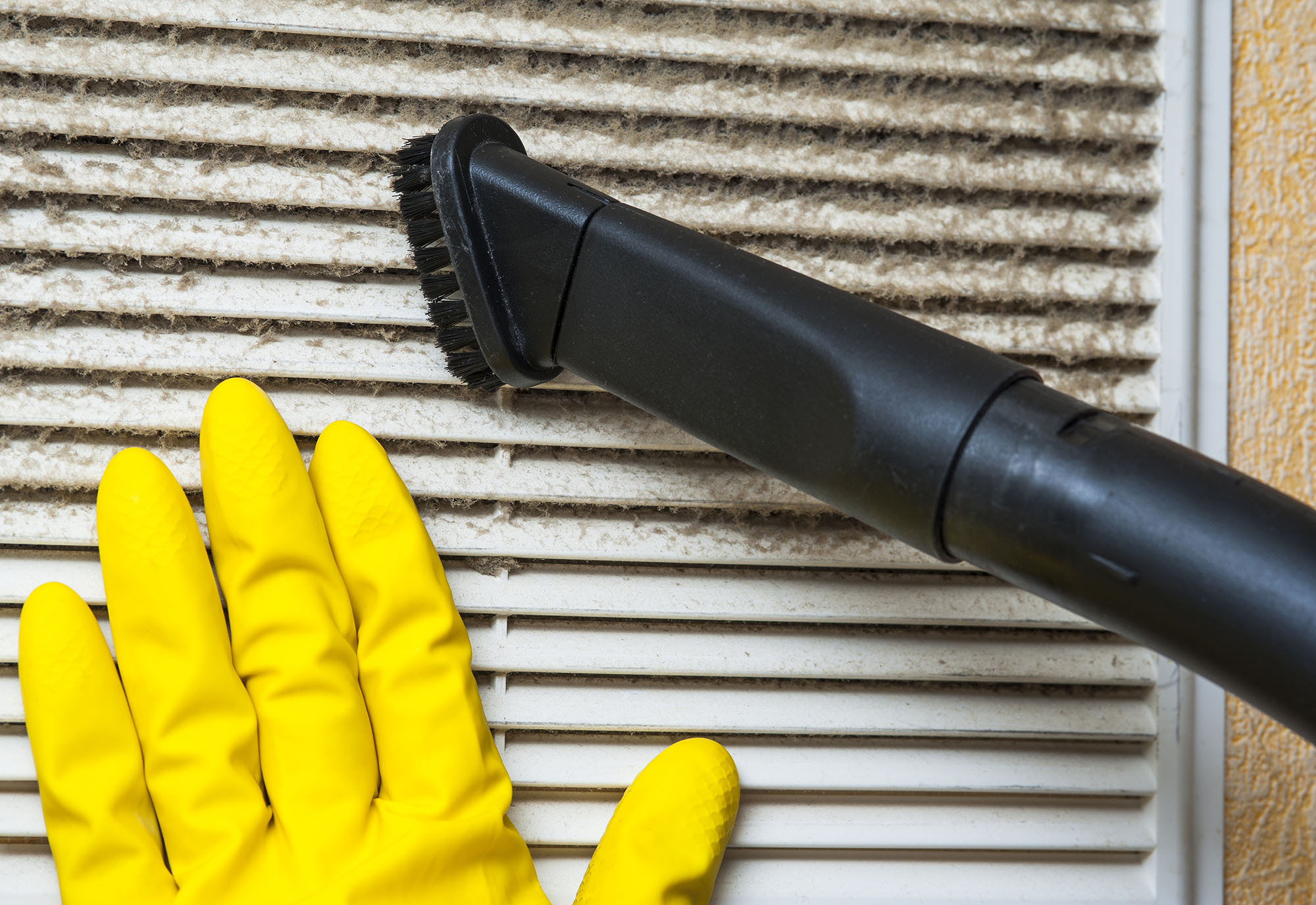 Person with yellow glove pressed up against HVAC system filter as they clean it with a vacuum brush.
