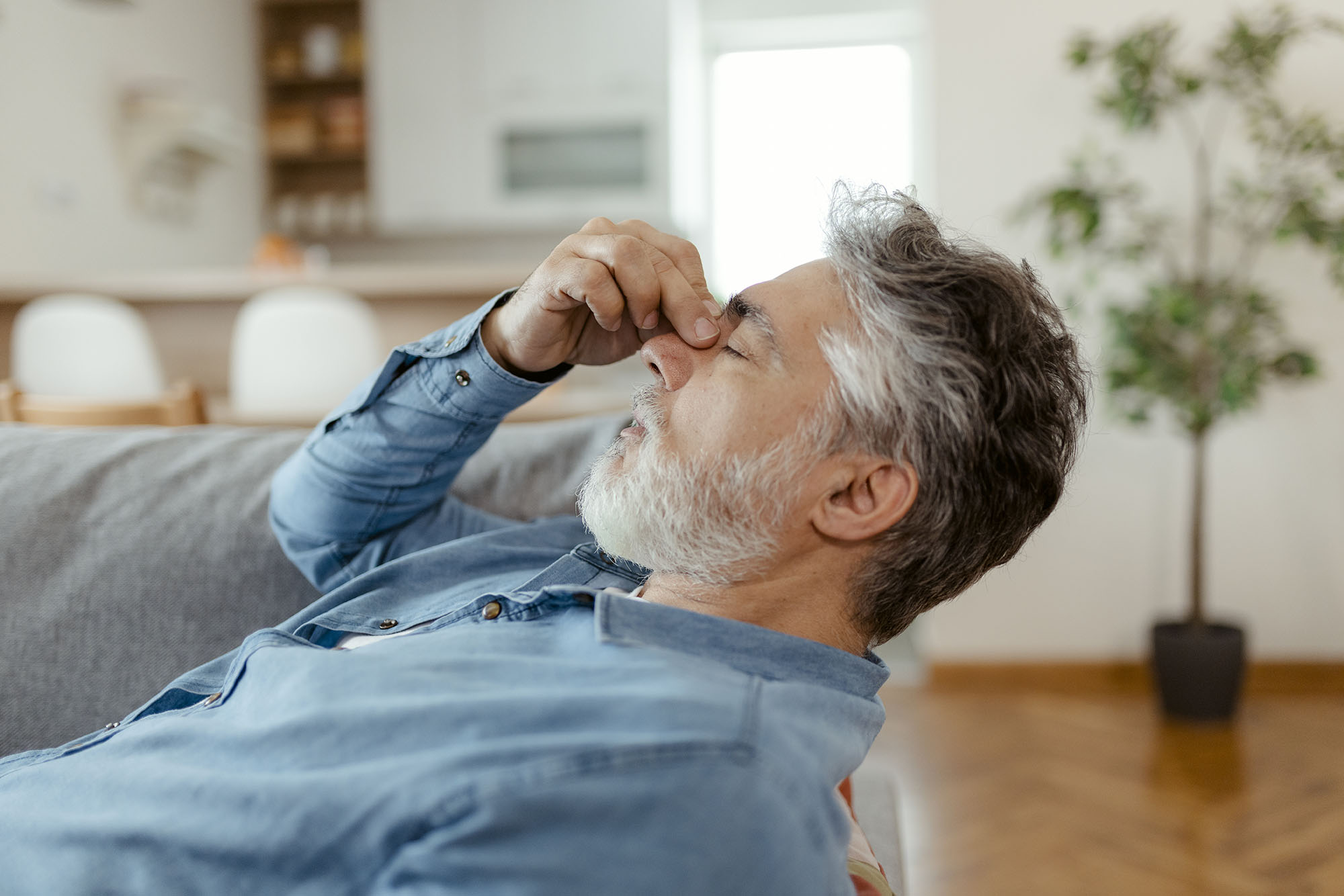 Man displaying aggravation with noise pollution at home by pinching his nose.