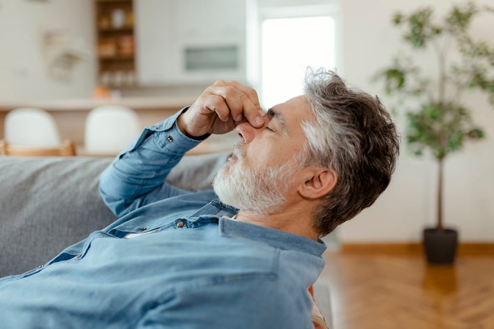Man displaying aggravation with noise pollution at home by pinching his nose.