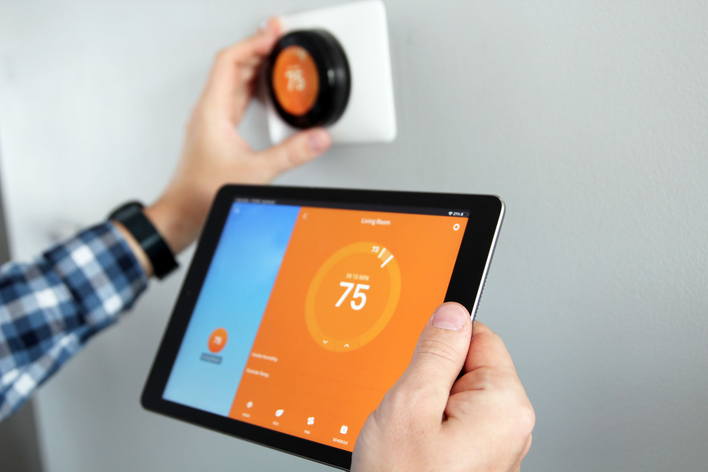 Person holding a tablet while setting up a smart thermostat in the home to help reduce the energy bill in the home during winter.