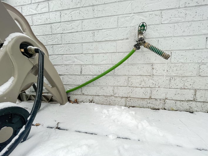 A garden hose attached to a spigot with snow on the ground, putting the house at risk ofwater damage.