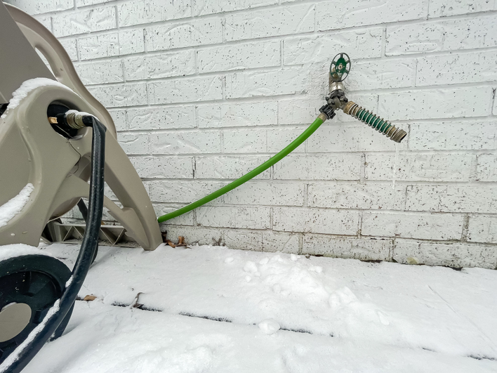 A garden hose attached to a spigot with snow on the ground, putting the house at risk of
water damage.
