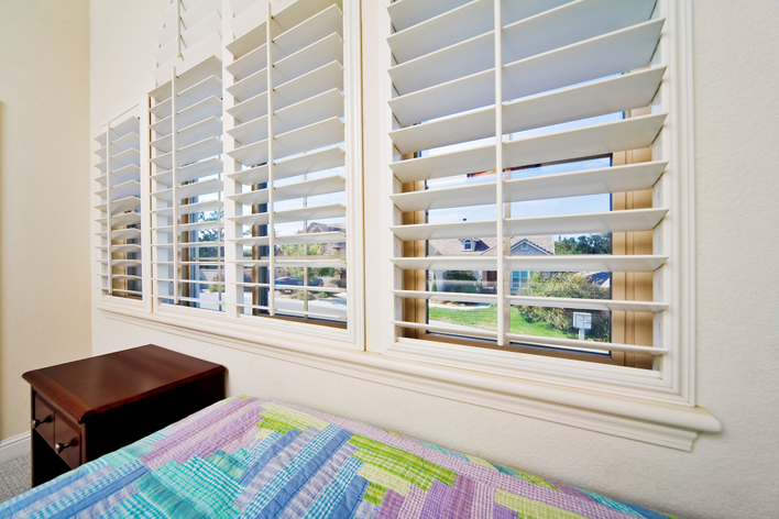 White plantation shutters provide a pet-proof window treatment in a white-walled bedroom.