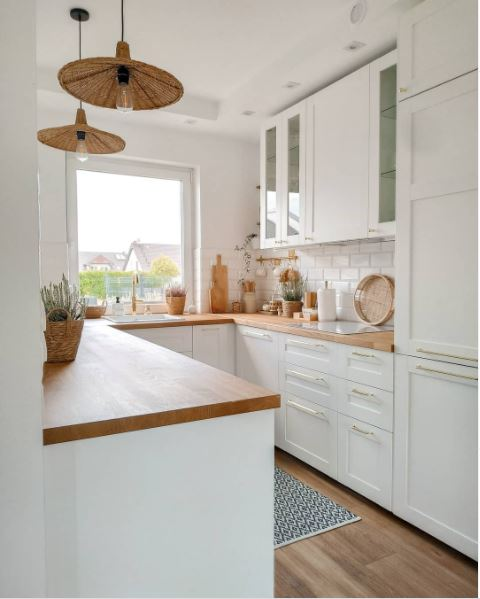 A charming kitchen in white with a large picture window and butcher block countertop