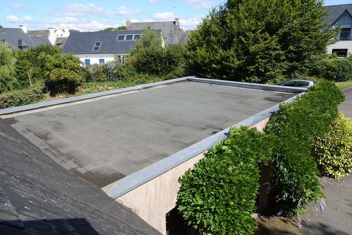 The flat roof of a building with trees and bushes around it.