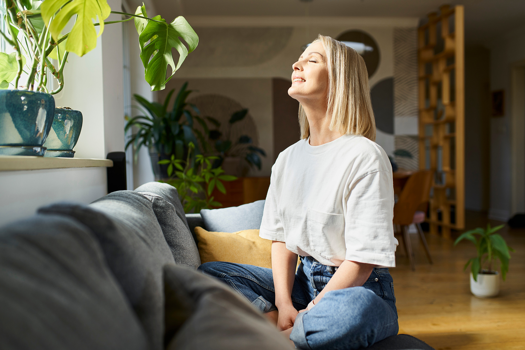 A woman enjoying the benefits of natural light as she faces the sun inside her home.