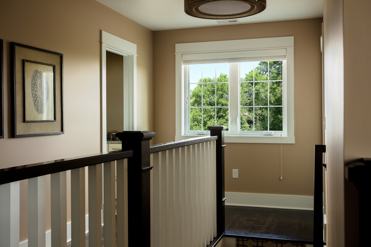 casement windows with colonial grids bring in daylight to an upstairs hallway, enhancing warm wall tones and classic white trim