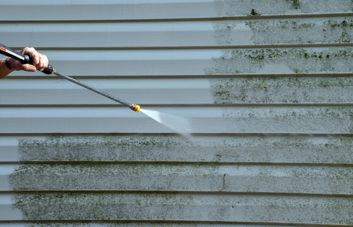 Person pressure washing their home’s siding.