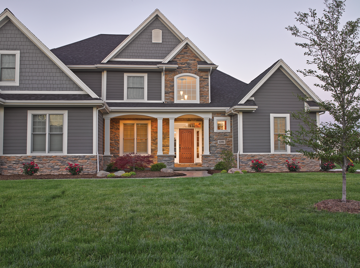 Large gray-colored home with custom windows and a wooden entry door.