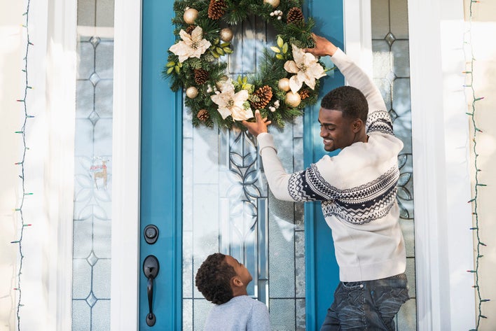 A man showing a child the best way to hang a wreath on a door.