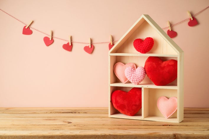 Simple Valentine’s Day decorations for home, including red and pink heart-shapedpillows in a wooden, house-shaped box and a garland of felt hearts.