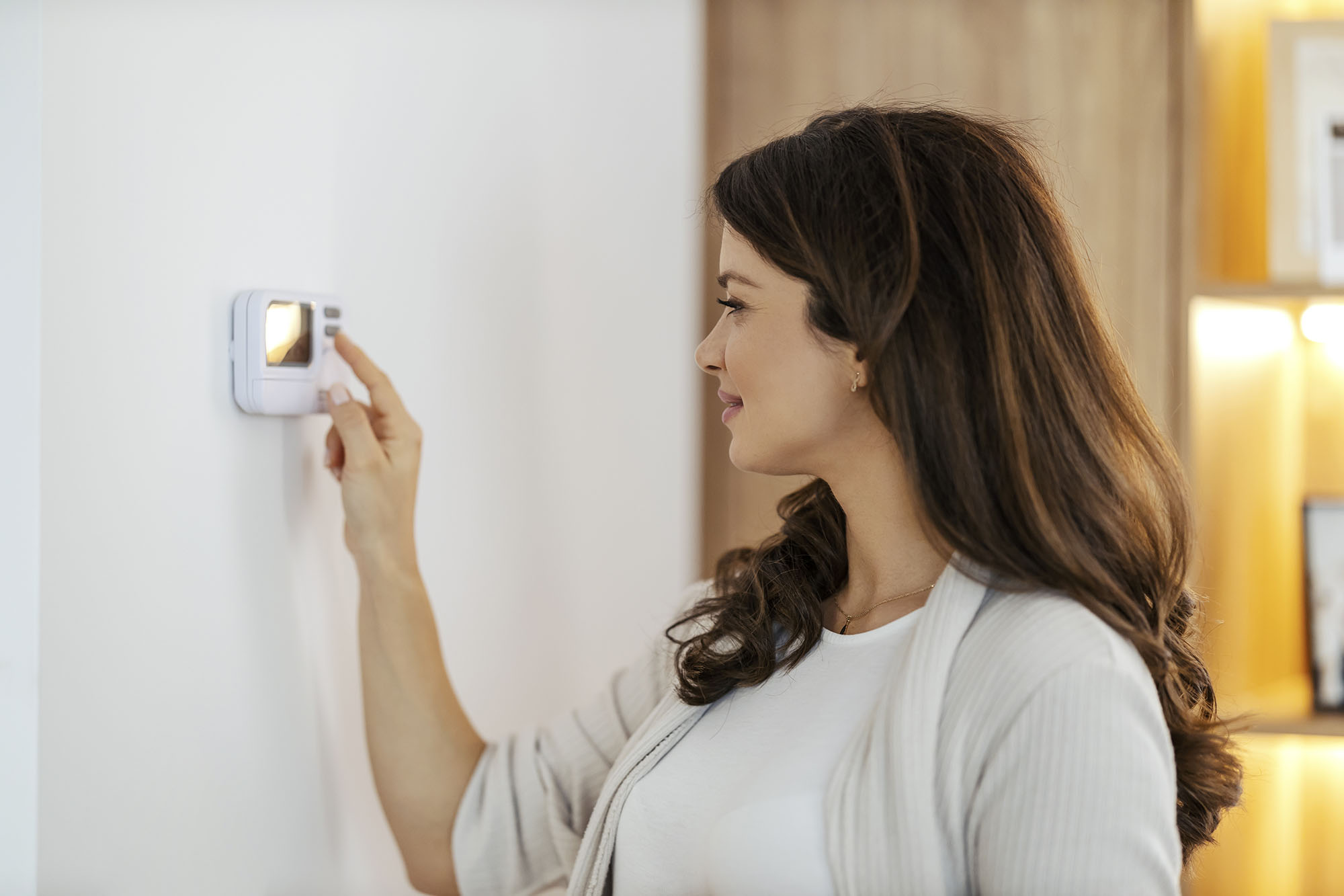 A smiling woman adjusting her home’s thermostat for the winter months.