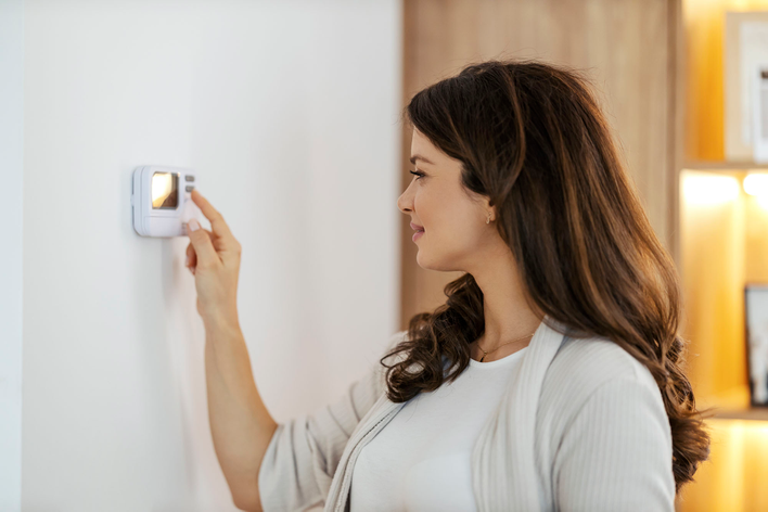 A smiling woman adjusting her home’s thermostat for the winter months.